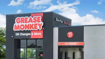 A Grease Monkey oil change service center with signage reading "Oil Changes & More" and "Done Fast. Done Right." under a clear blue sky.