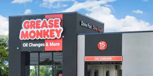 A Grease Monkey oil change service center with signage reading "Oil Changes & More" and "Done Fast. Done Right." under a clear blue sky.
