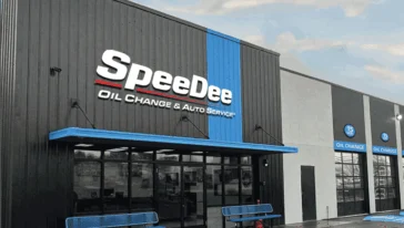 Exterior view of a SpeeDee Oil Change & Auto Service building with large signage, glass entrance doors, and blue benches near the entrance.
