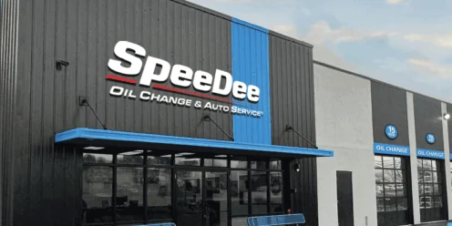 Exterior view of a SpeeDee Oil Change & Auto Service building with large signage, glass entrance doors, and blue benches near the entrance.