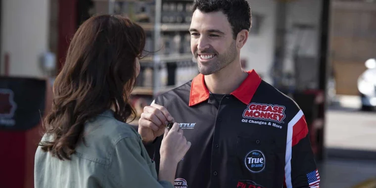 A woman hands car keys to a smiling mechanic wearing a Grease Monkey uniform at an automotive service shop.