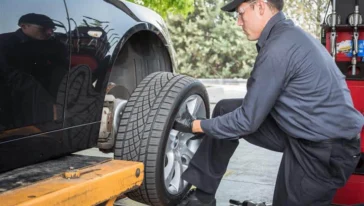 A mechanic in uniform installs a tire onto a car lifted on a hydraulic platform at an auto repair shop.
