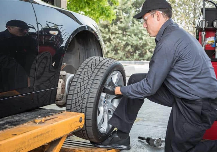 A mechanic in uniform installs a tire onto a car lifted on a hydraulic platform at an auto repair shop.