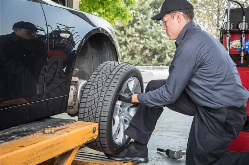 A mechanic in uniform installs a tire onto a car lifted on a hydraulic platform at an auto repair shop.