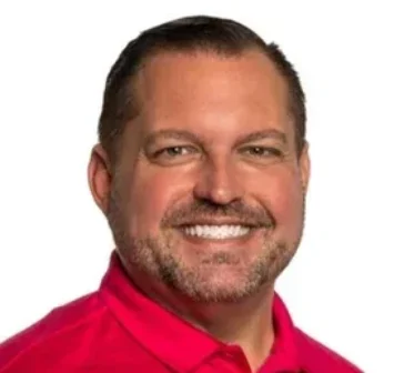 Harry Jenkins with short dark hair, beard, and mustache, wearing a bright red collared shirt, pictured against a plain white background.