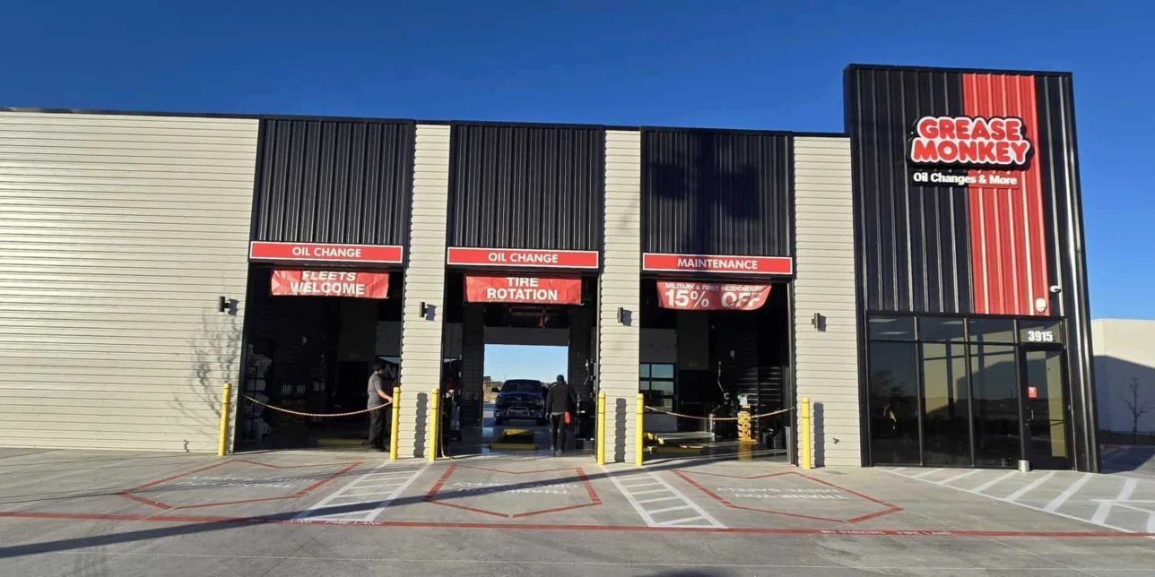 A Grease Monkey auto service center with three service bays, signage for oil change, tire rotation, maintenance, and a 15% off offer visible above the open garage doors.