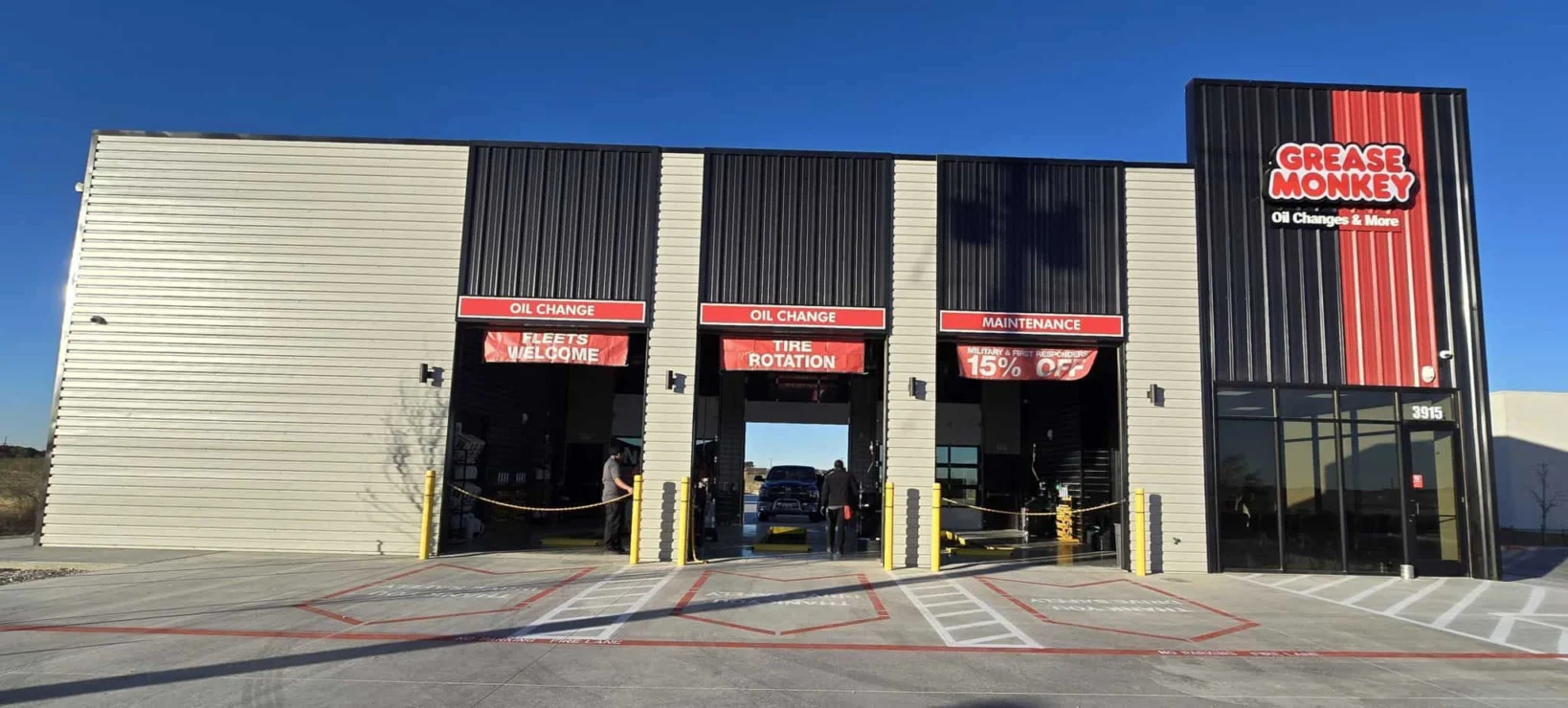 A Grease Monkey auto service center with three service bays, signage for oil change, tire rotation, maintenance, and a 15% off offer visible above the open garage doors.